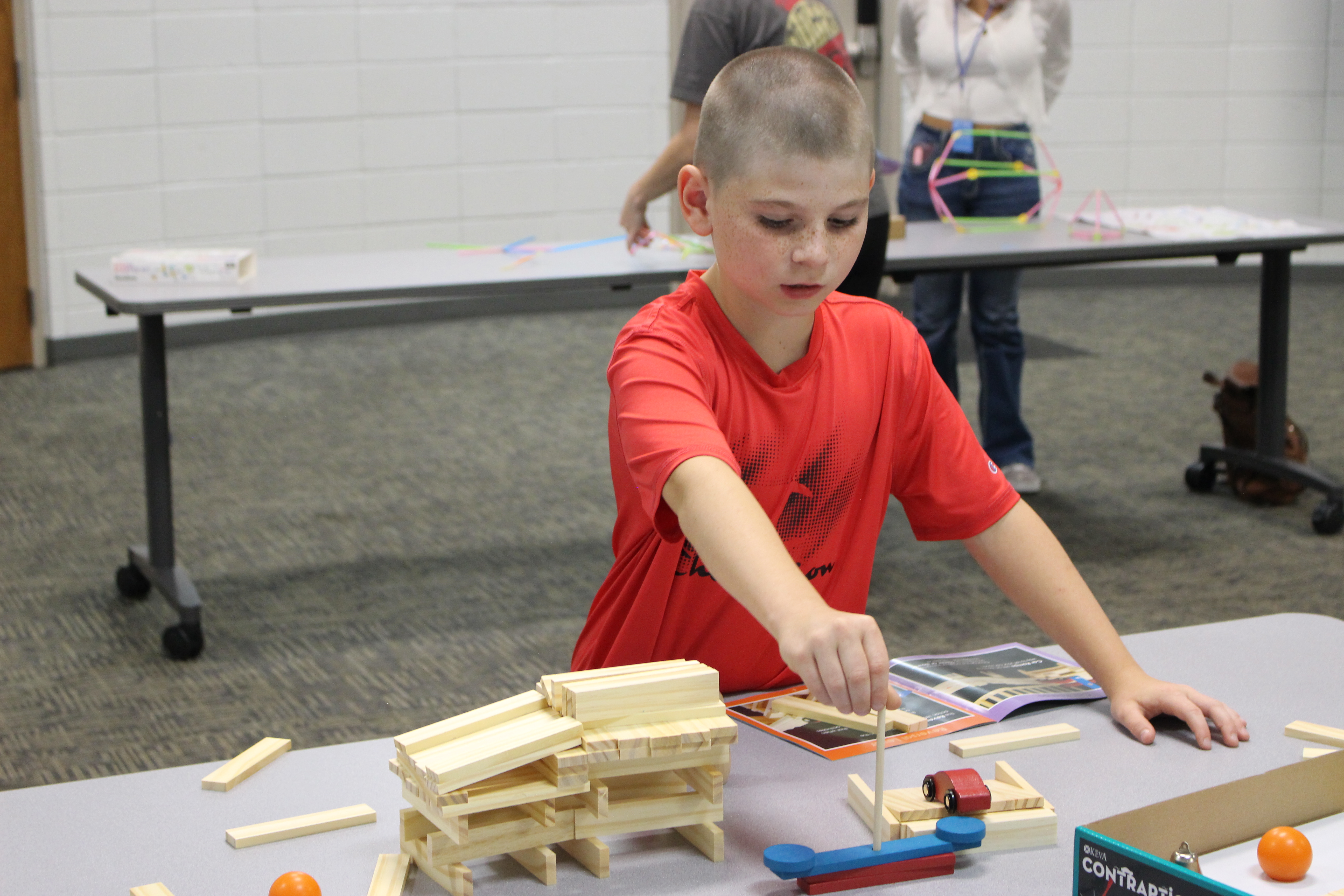 A tween at a CCJPL tween event builds with blocks and dowels to create a track for a toy car